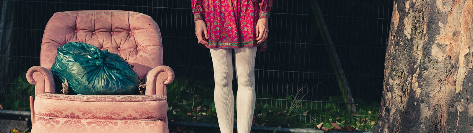 A young woman is standing next to an old armchair outside on the grass