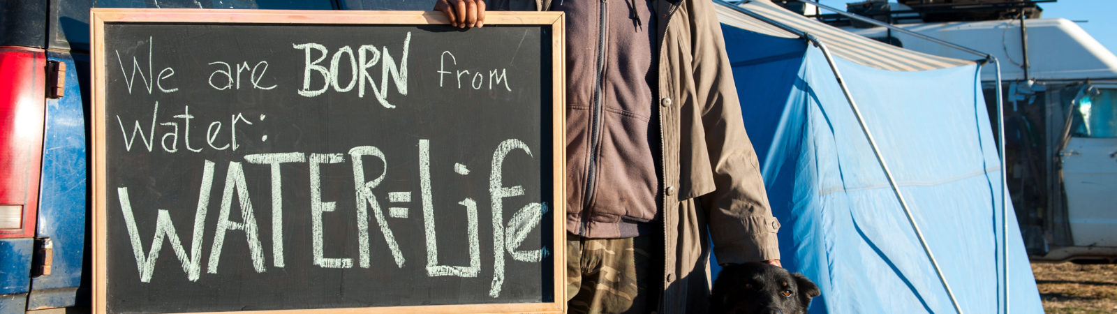 Man standing with chalkboard with the words, Water=Life