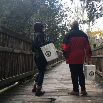 Two people stand on Northland College bridge with composting buckets.