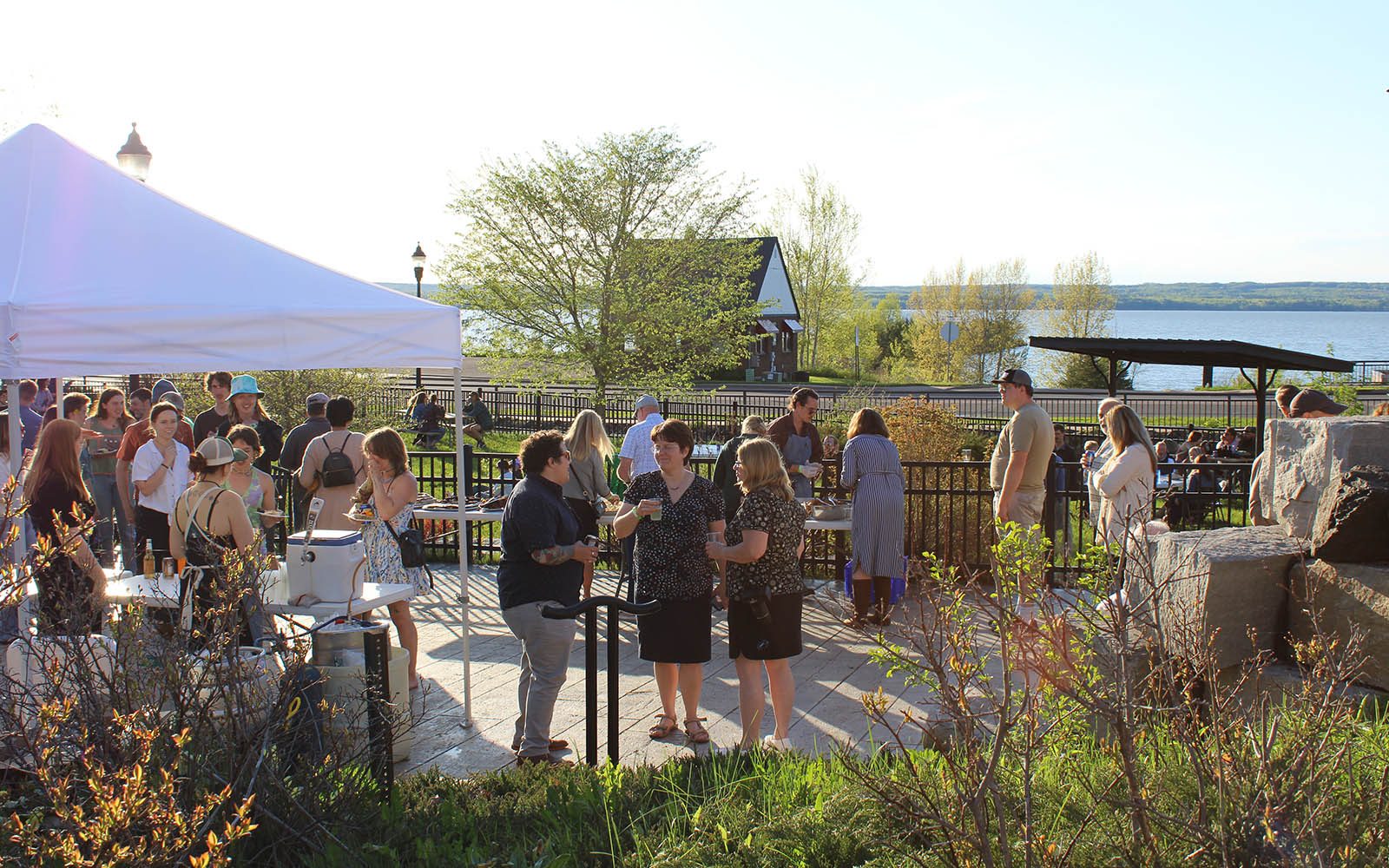 Graduates, their friends and family, and members of the campus community mill about at the Confluence with Lake Superior in view