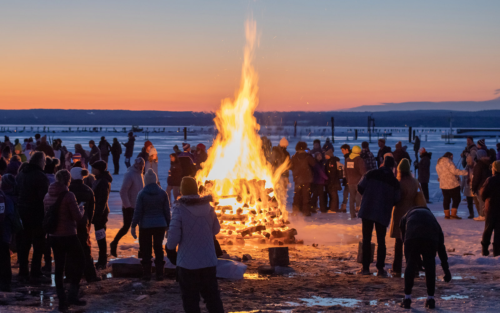 People are congregated around a roaring bonfire on the ice of Chequamegon Bay at Book Across the Bay festivities
