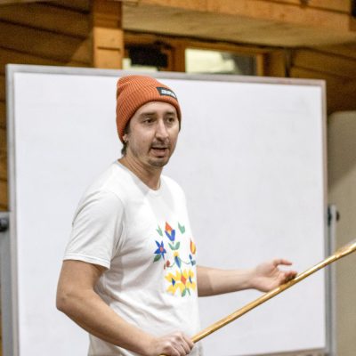Dylan Bizhikiins Jennings giving a talk with a snow snake
